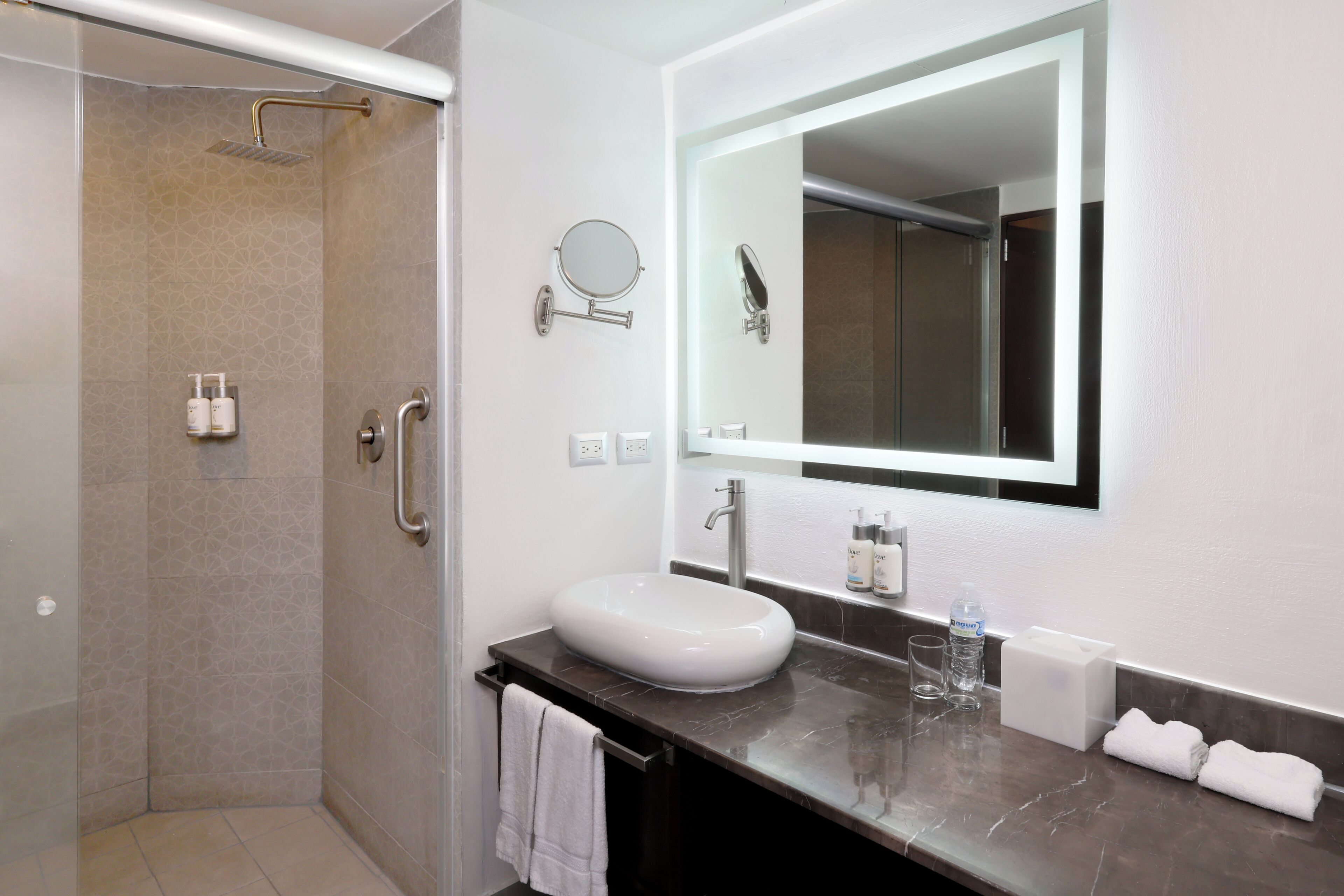 A modern bathroom with a glass-enclosed shower, a white sink, a large mirror, and a marble countertop.