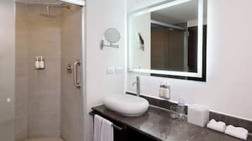 A modern bathroom with a glass-enclosed shower, a white sink, a large mirror, and a marble countertop.