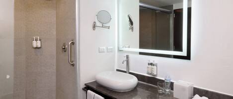 A modern bathroom with a glass-enclosed shower, a white sink, a large mirror, and a marble countertop.