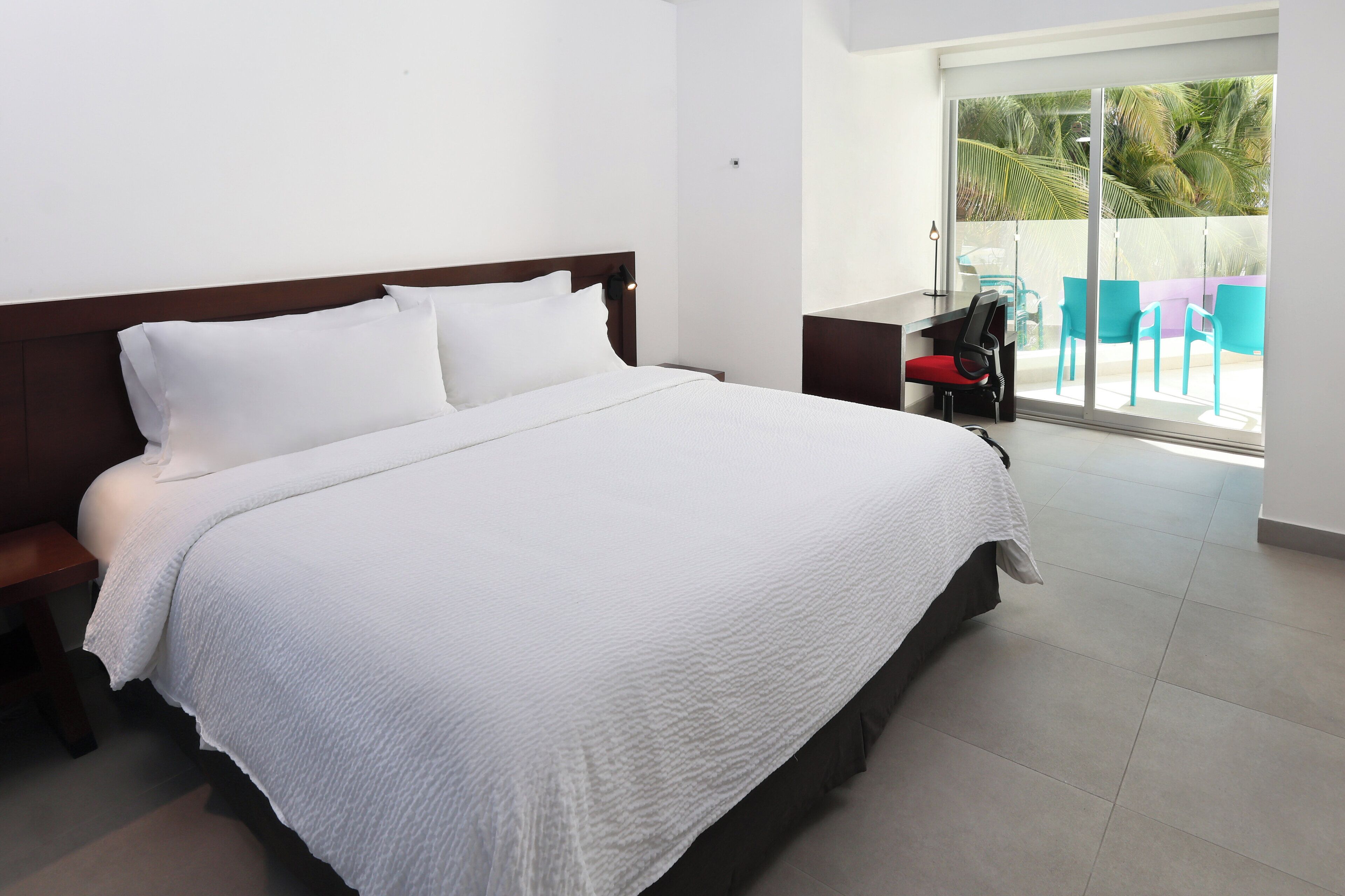 Een netjes opgemaakt bed met een witte dekbedovertrek in een moderne hotelkamer met een groot raam en uitzicht op palmbomen.