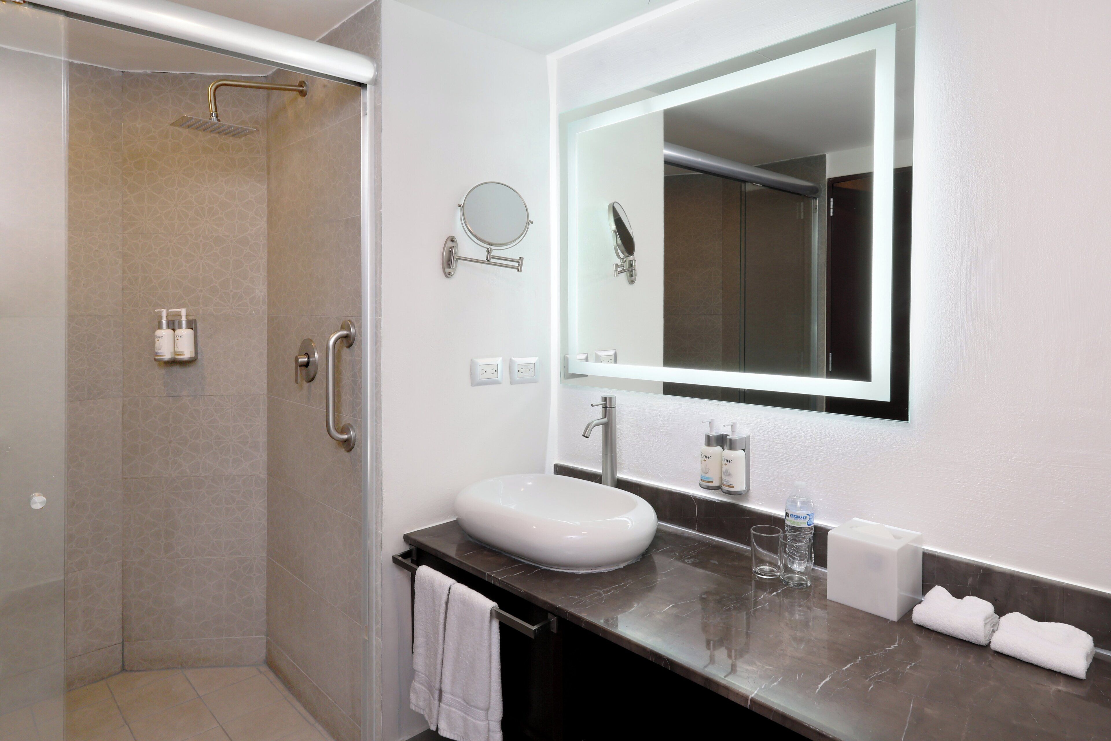 A modern bathroom with a glass-enclosed shower, a white sink, and a large mirror.