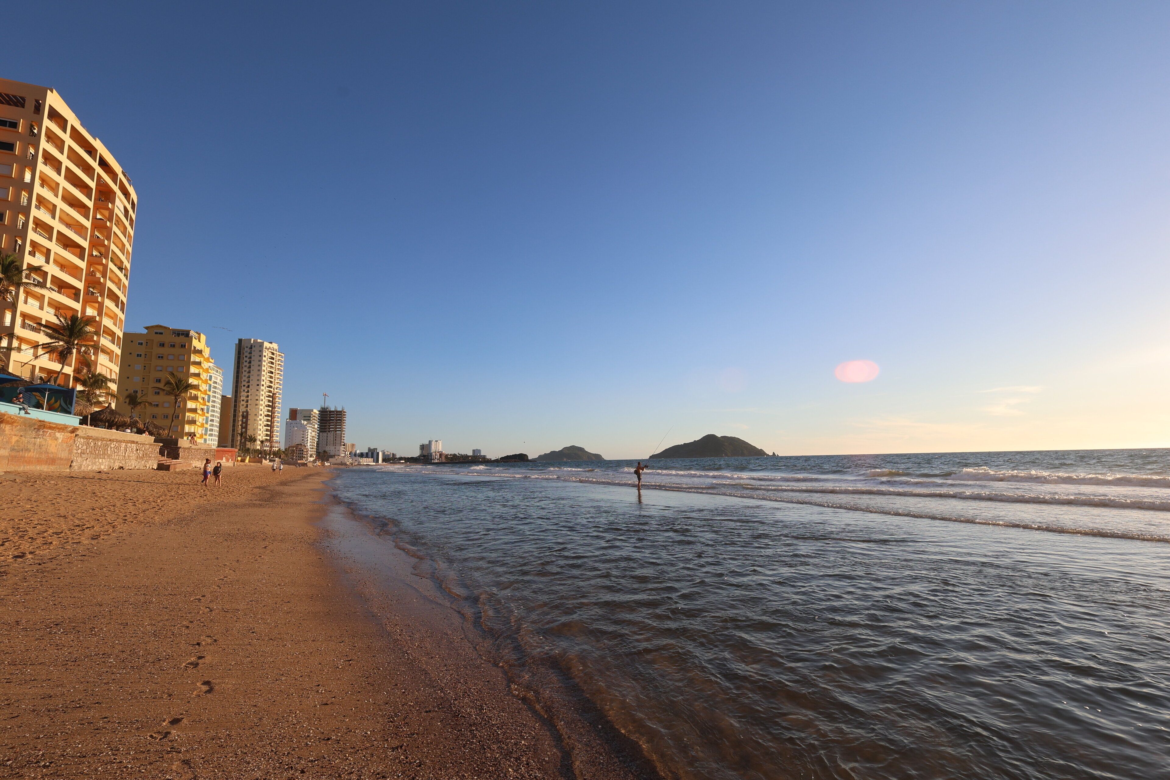 A beach with a sandy shore, a few people, and buildings in the background.