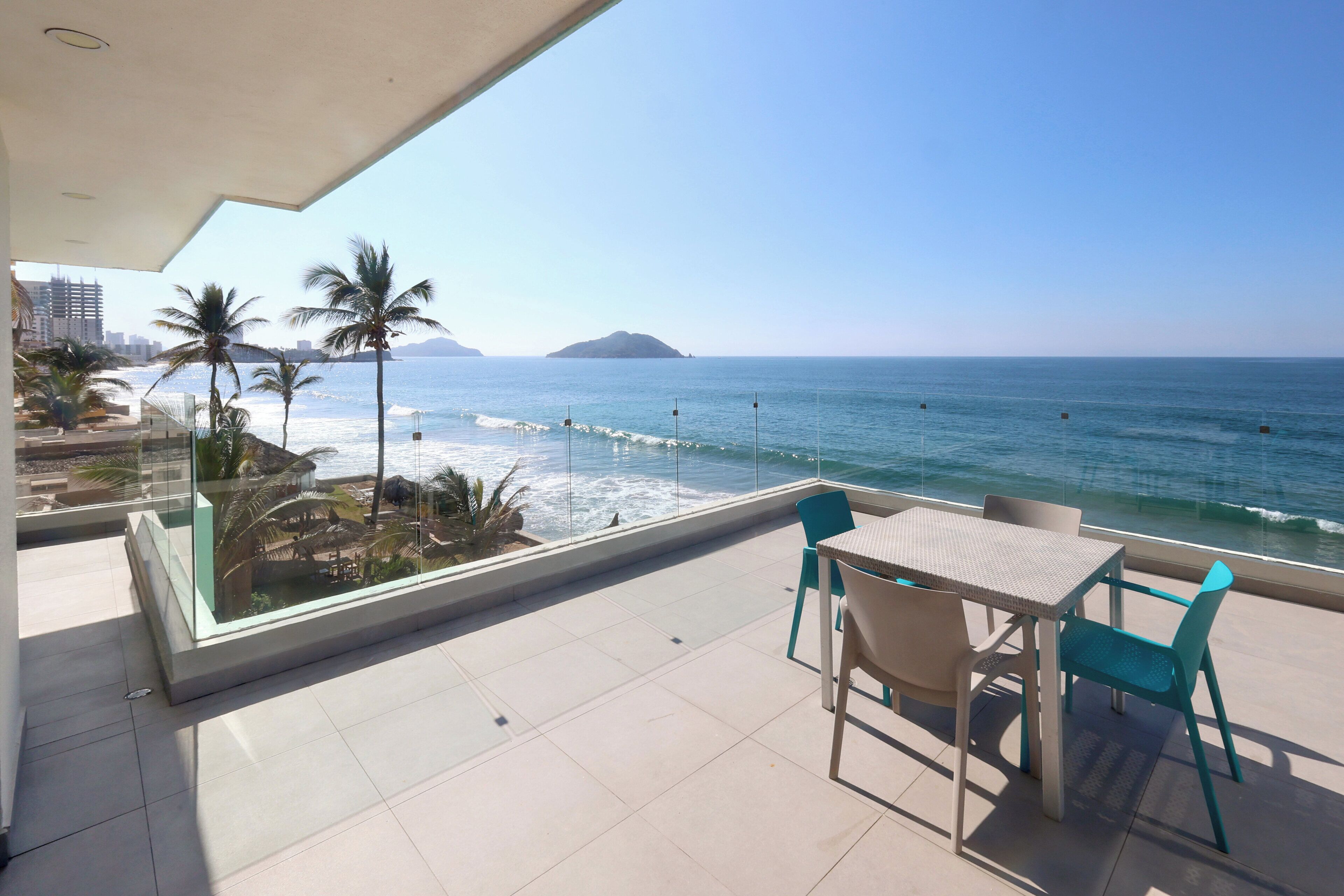 A balcony with a view of the ocean, a table, and chairs.