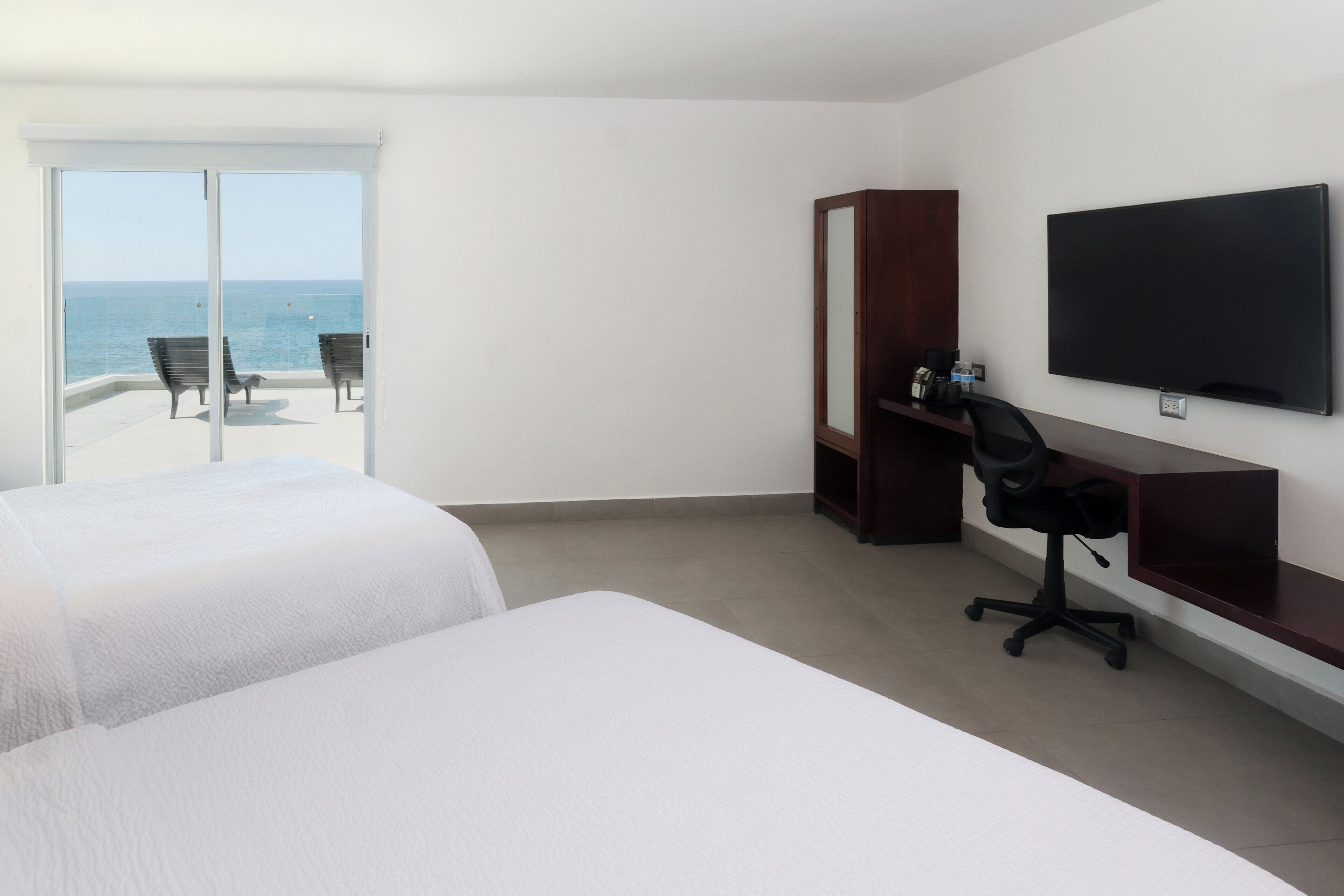 A hotel room with two beds, a desk with a chair, a TV, and a sliding glass door to the balcony.