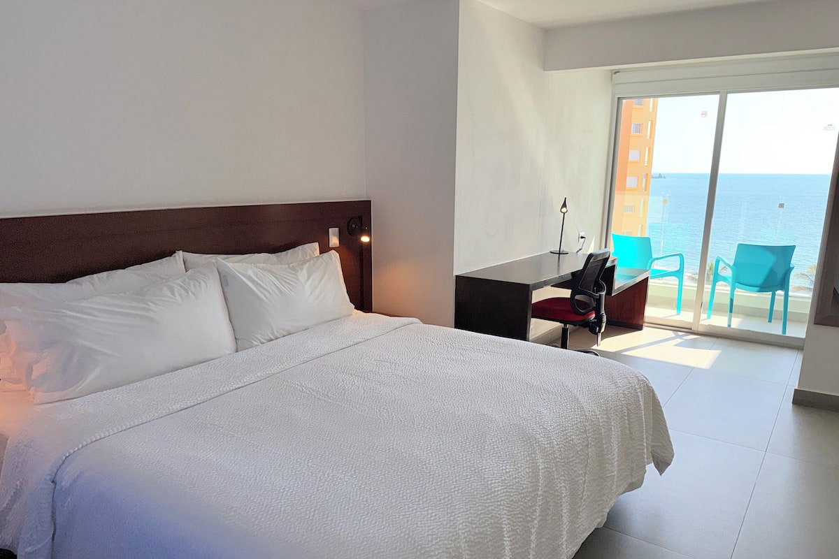 Una habitación de hotel con una cama grande, un escritorio y vistas al mar.