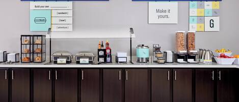 A buffet setup with labeled food stations, a coffee machine, and a fruit bowl.