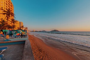 Una playa con un paseo de concreto, palmeras y un mural colorido.