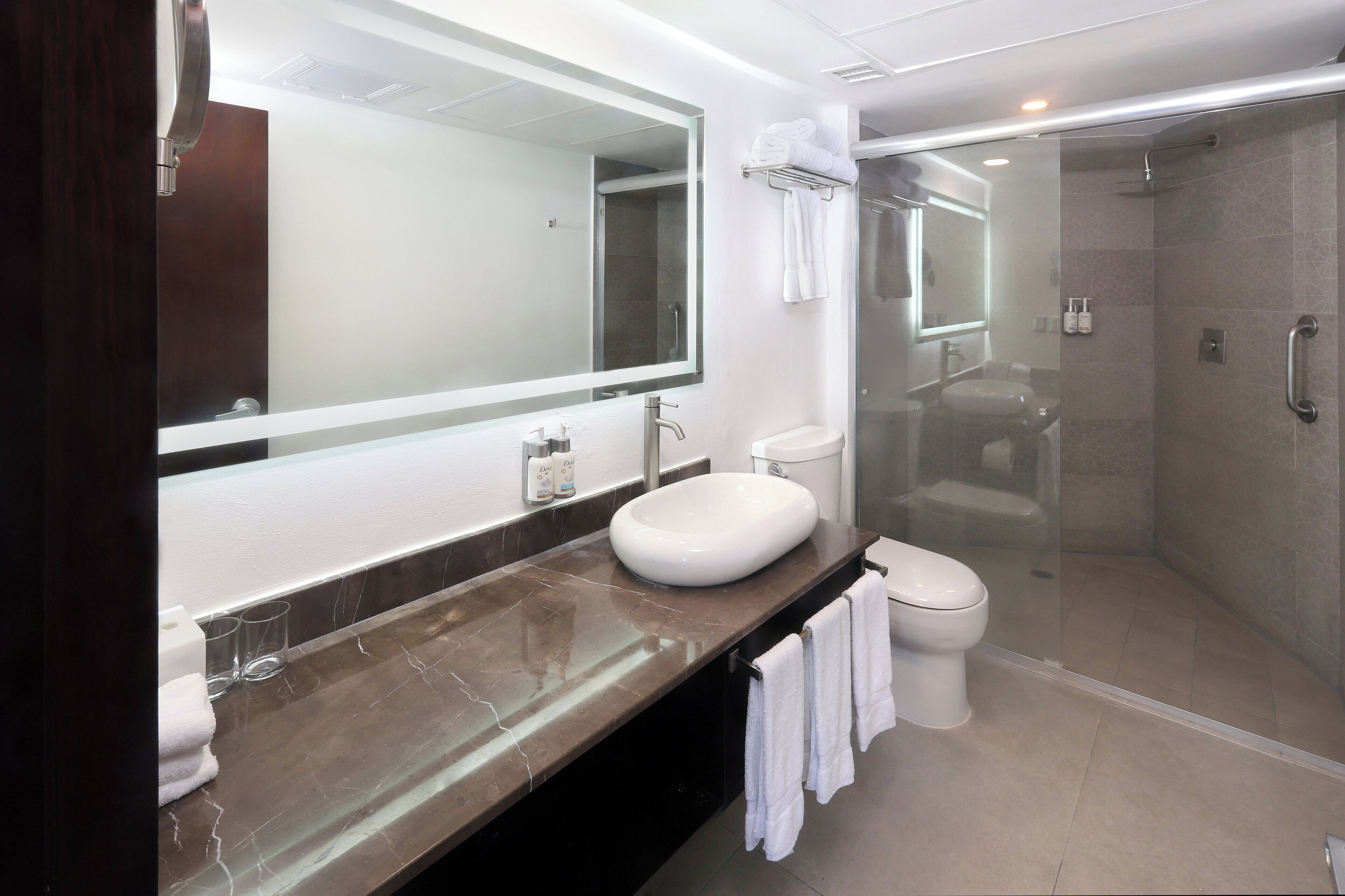 A modern bathroom with a large mirror, a white sink, a glass-enclosed shower, and a toilet.