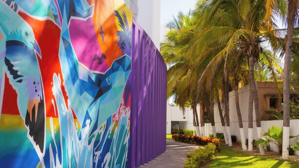 Une fresque colorée sur un bâtiment, un sentier et des palmiers.