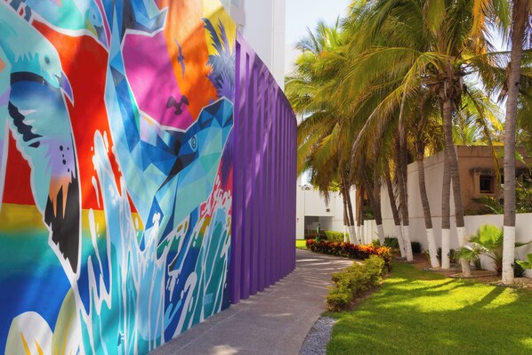 A colorful mural on a building, a pathway, and palm trees. - Garner Hotel Mazatlan Beach by IHG (Mazatlán)