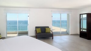 Une chambre d’hôtel avec un grand lit, un fauteuil avec des coussins, une télévision et un balcon donnant sur la mer.