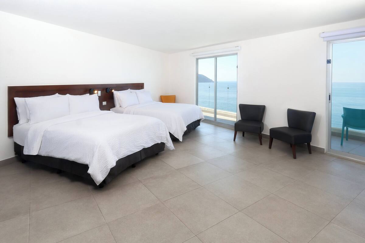 Habitación de hotel con dos camas, zona de estar y vista al mar.
