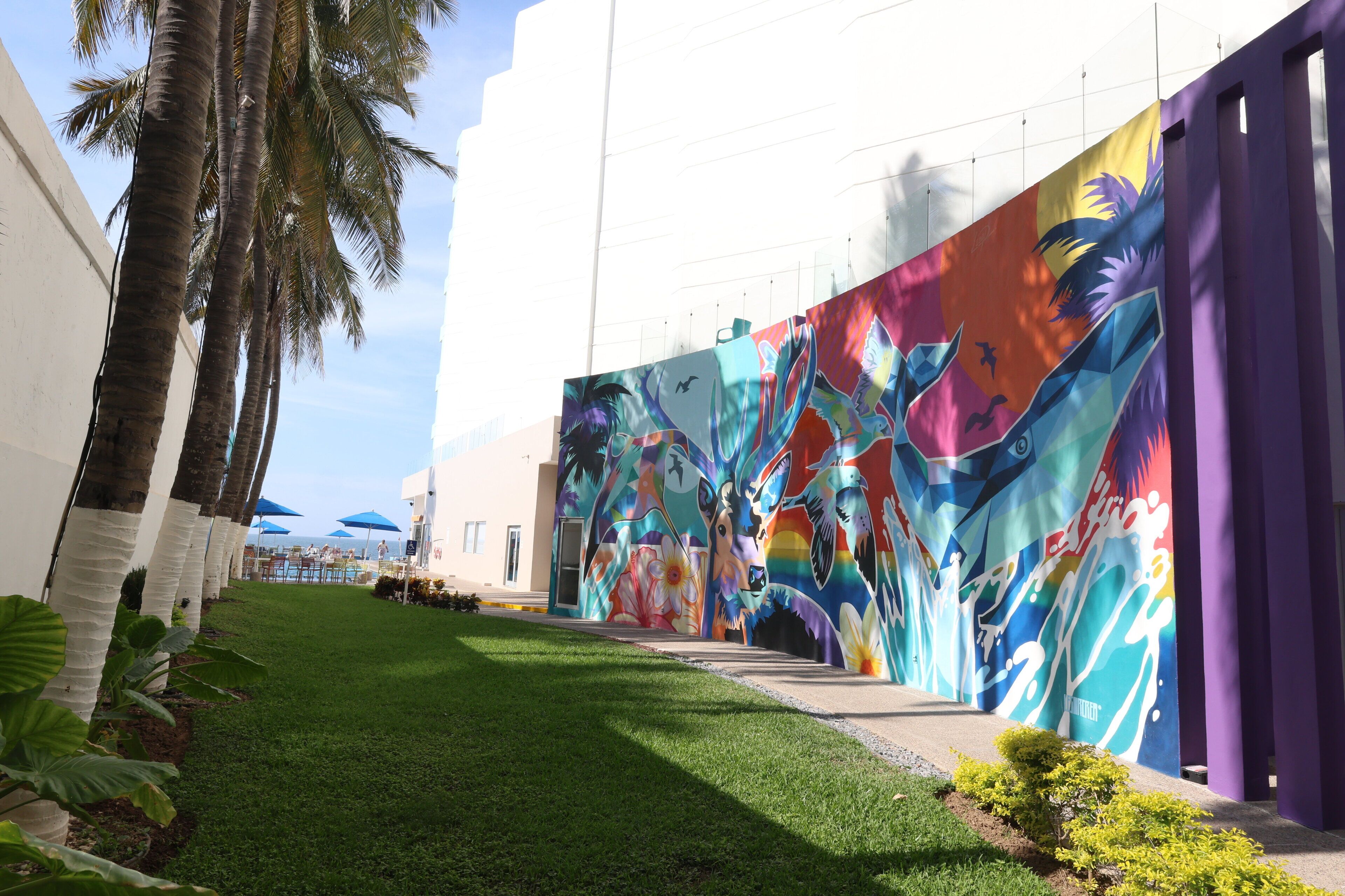 A building with a colorful mural on the side, a well-maintained lawn, and palm trees.