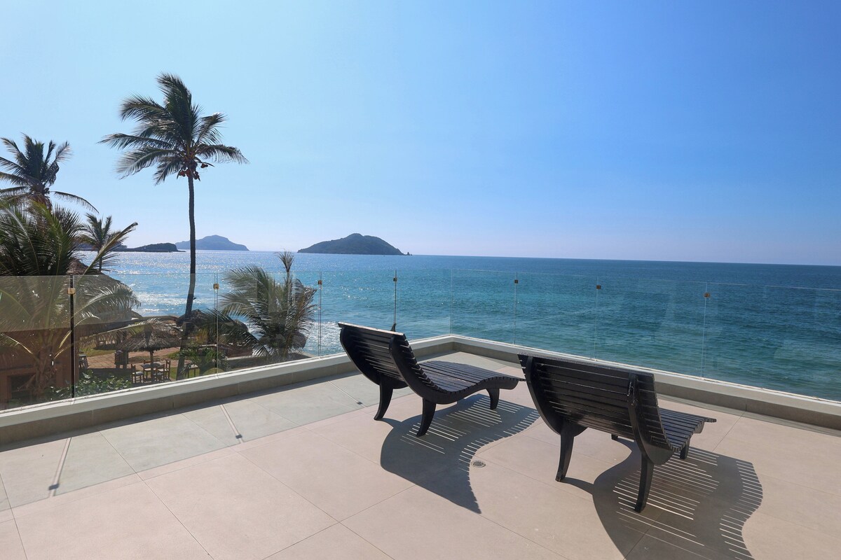 A balcony with two black benches overlooking a clear blue sea and a distant island.