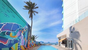 Un espace aménagé au bord de la piscine, agrémenté de peintures murales colorées, de chaises longues et offrant une vue sur l’océan.