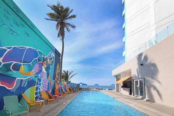 Zona de piscina con murales coloridos, sillones de descanso y vistas al océano.