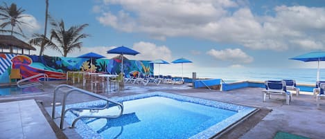 A pool area with lounge chairs and umbrellas, a slide, and a mural.