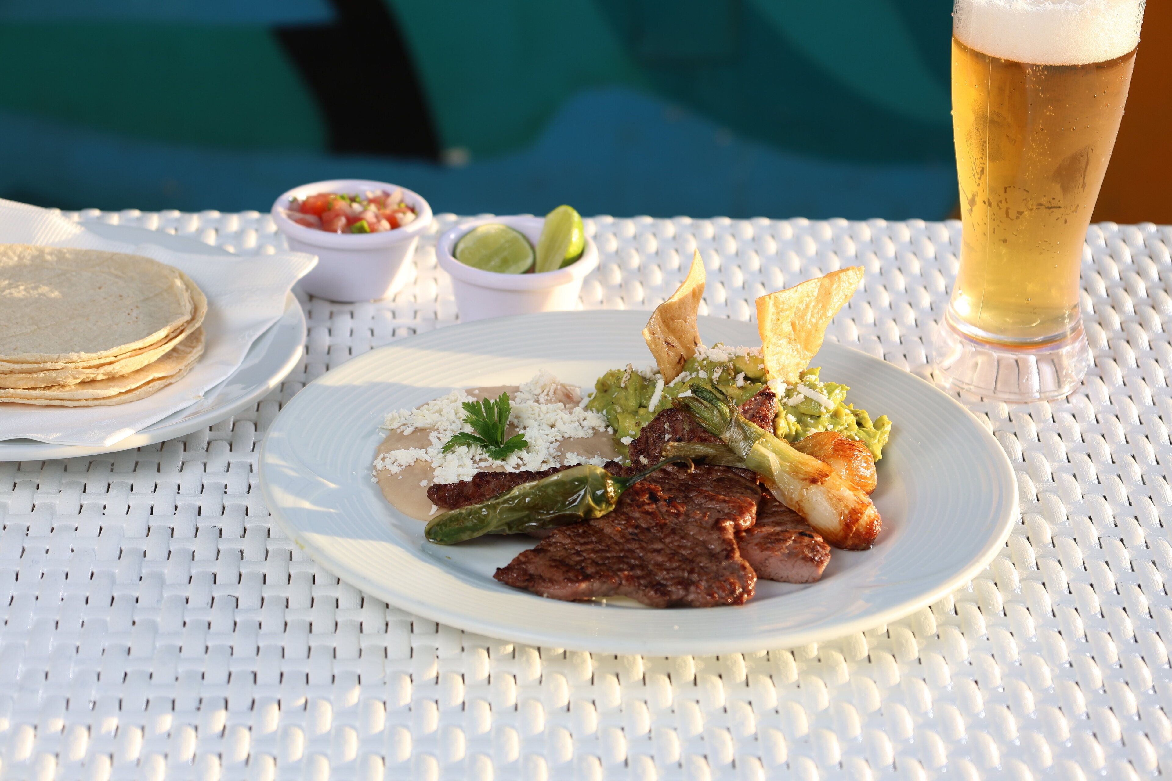 A dining table with a plate of food, a glass of beer, and small bowls of condiments.