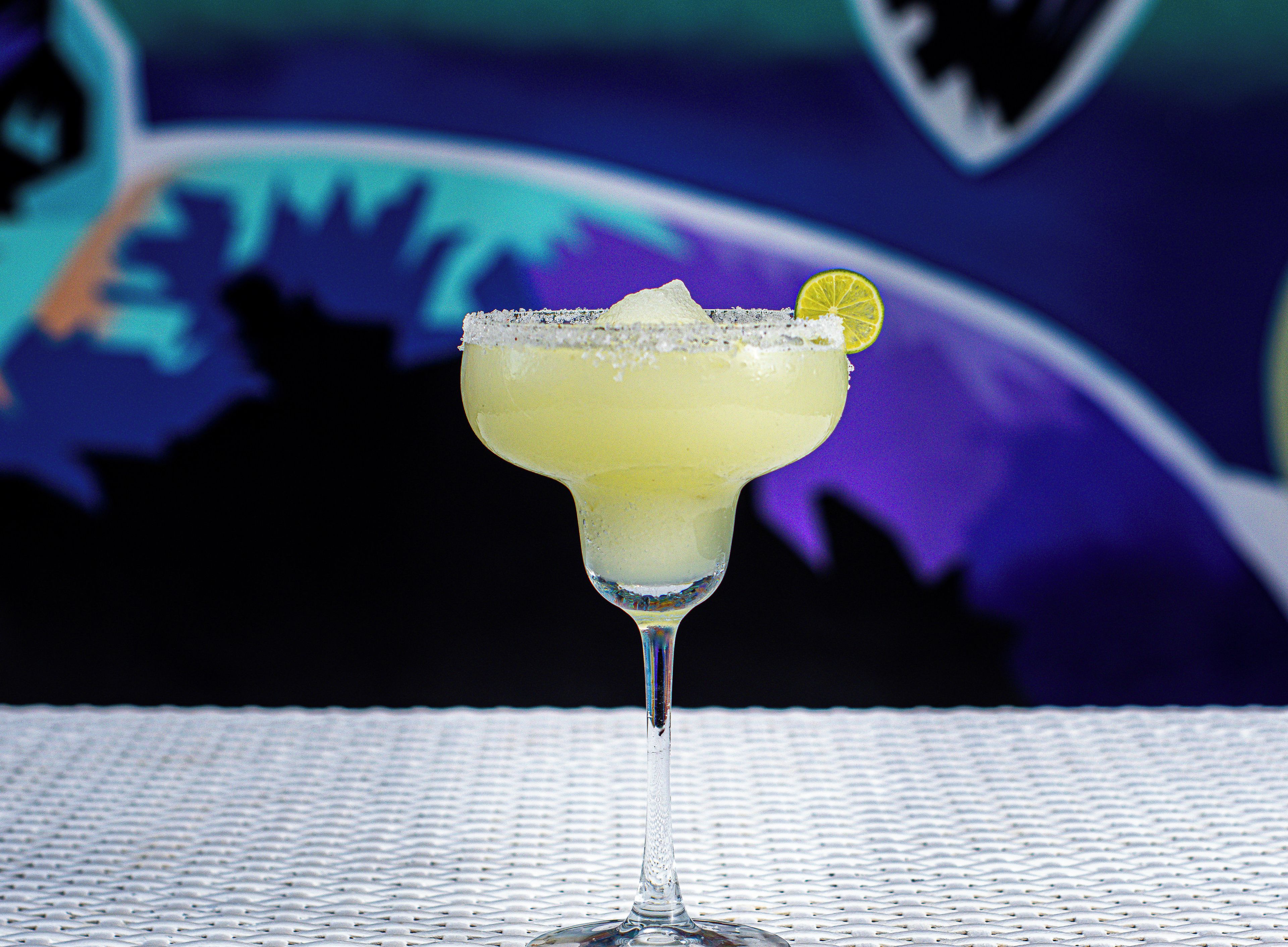 A margarita cocktail in a stemmed glass with a salted rim and a lime garnish, placed on a textured surface.