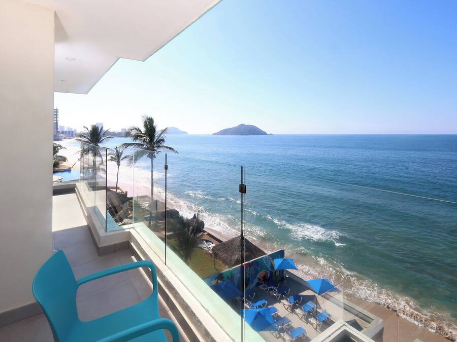 A balcony with a view of the sea, a lounge area with blue chairs and umbrellas, and a glass railing.