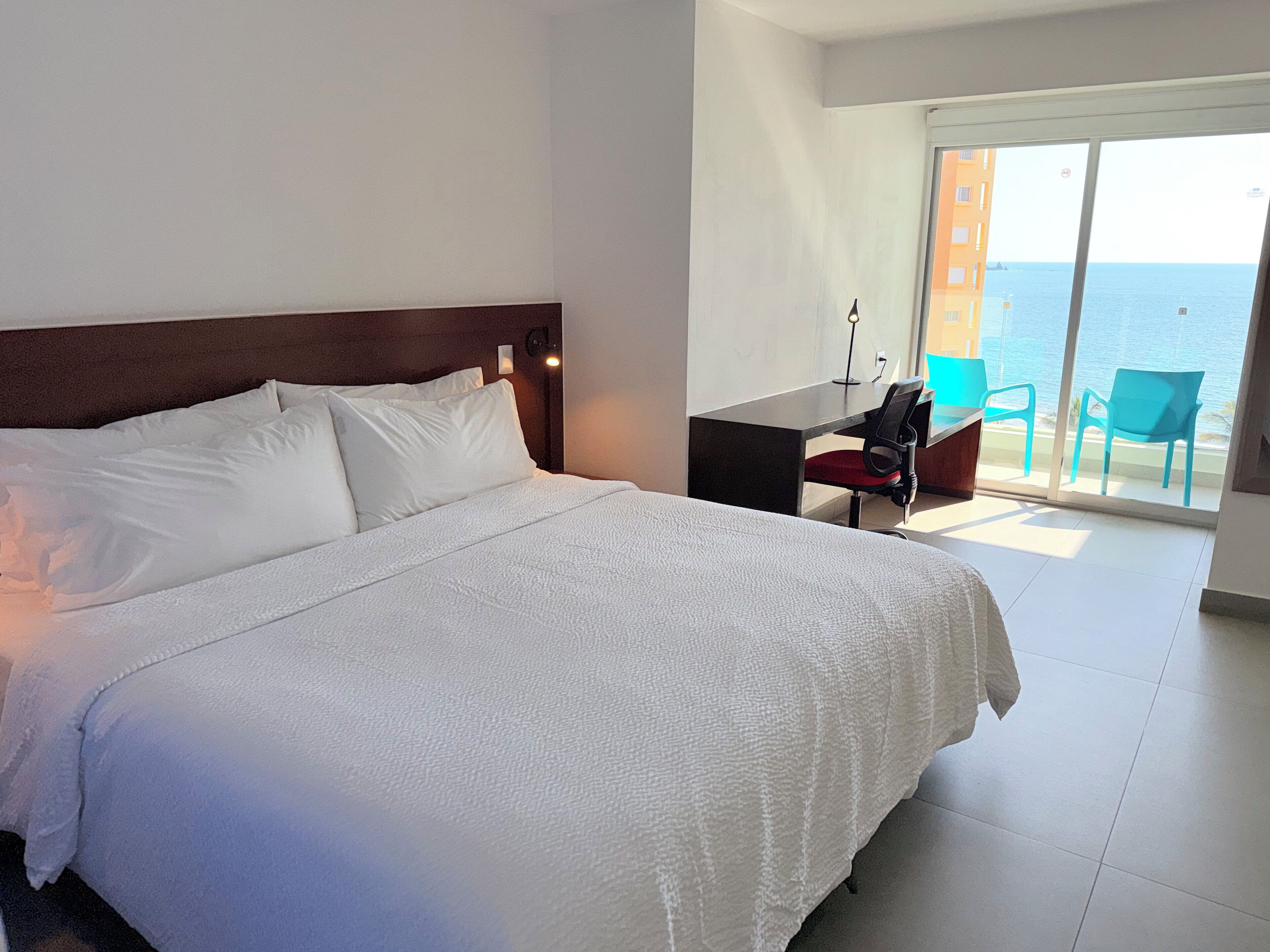 A hotel room with a large bed, a desk, and a view of the sea.