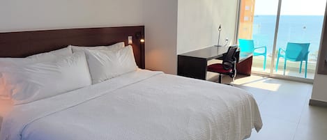 Ett hotellrum med en stor säng, ett skrivbord och utsikt över havet.