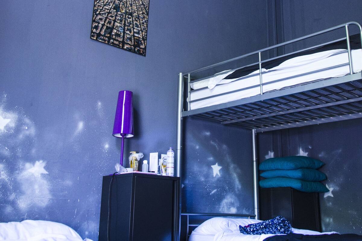 Huoneessa on kerrossänky, yöpöytä, jossa on lamppu, ja seinällä on kaksi kehystettyä kuvaa.