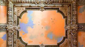 Un techo ornamentado con detalles en oro intrincados y una escena pintada del cielo.