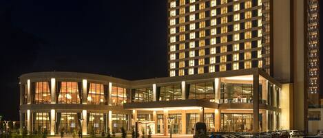 Un hotel de varios pisos con un diseño moderno, que destaca por una amplia fachada de vidrio y una entrada bien iluminada.