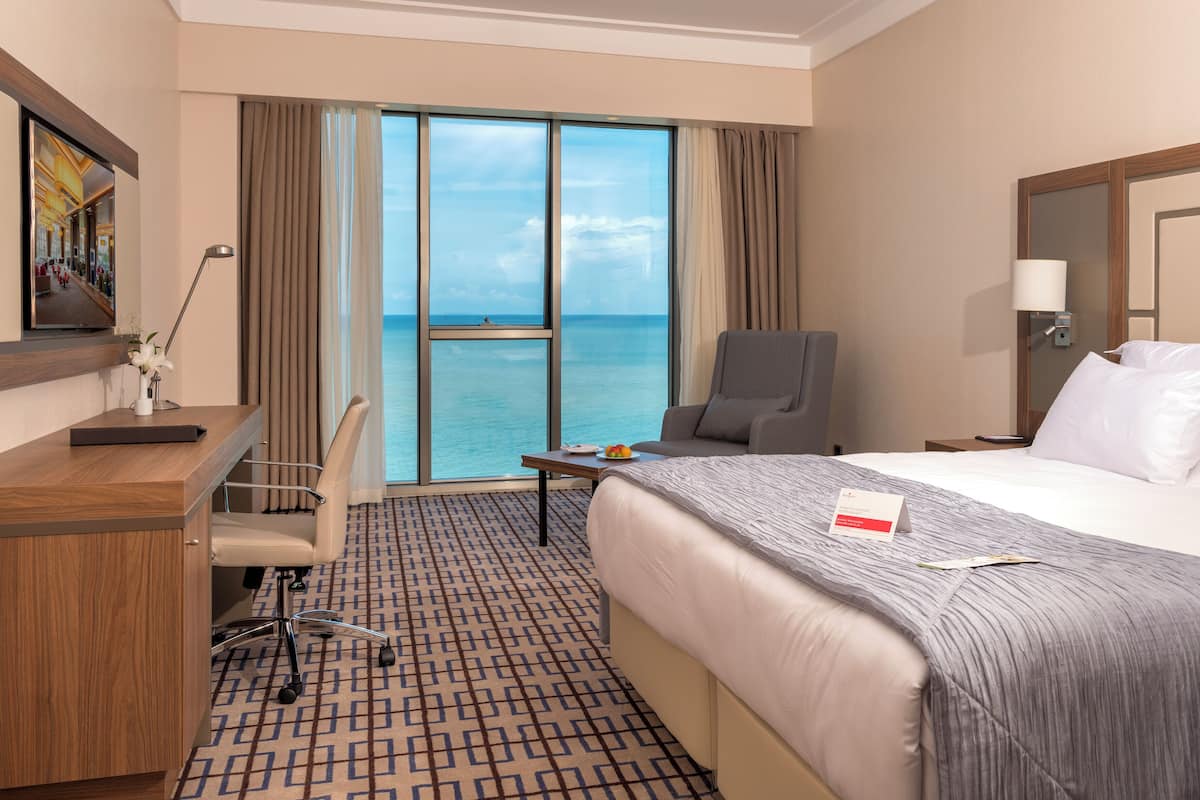 A hotel room with a large bed, a desk, a chair, and a view of the ocean.