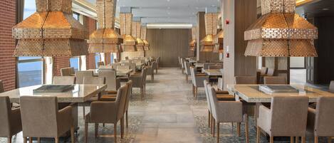 A spacious dining area with brick-patterned ceiling lights, numerous tables, and chairs arranged for dining.