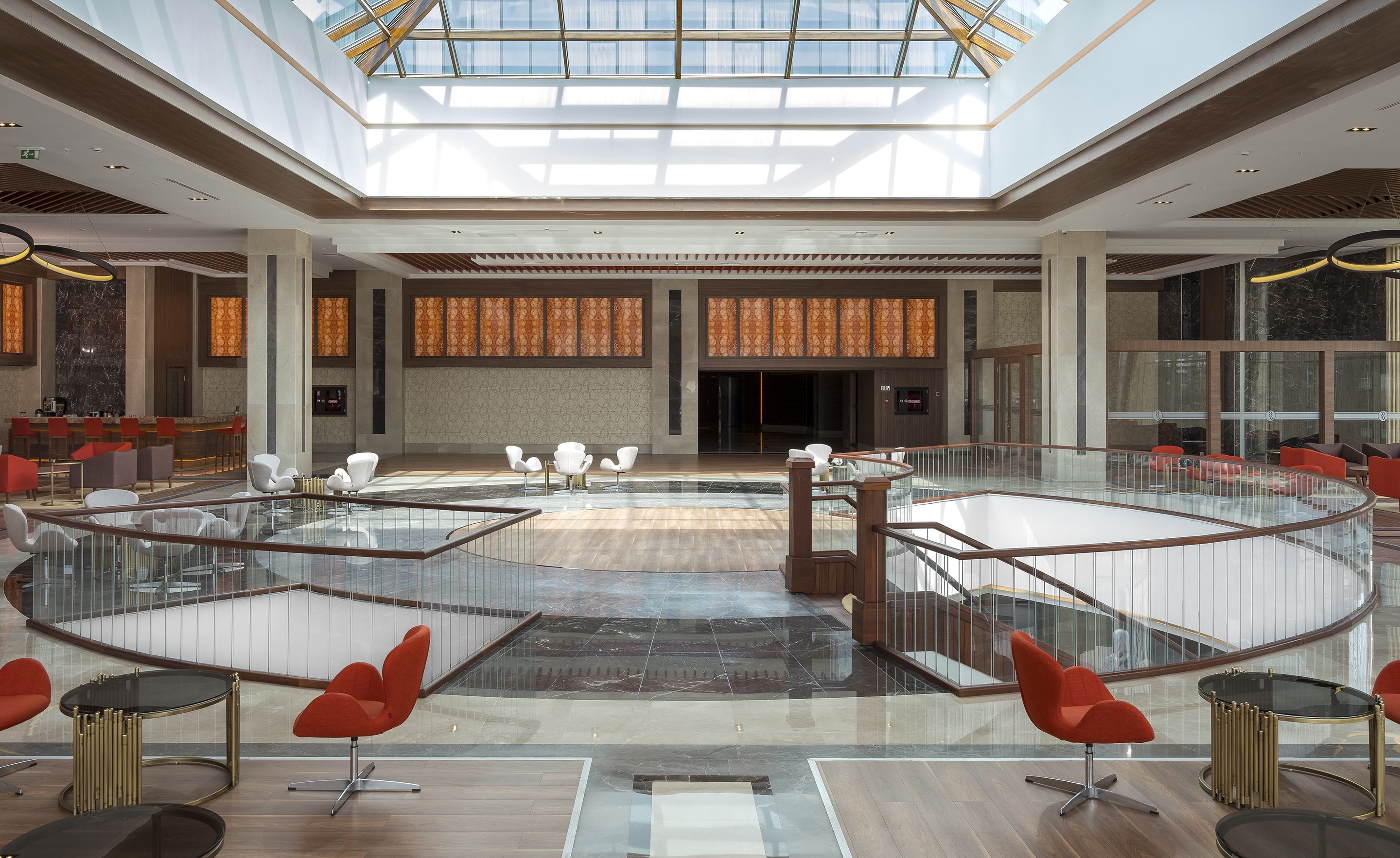Un hall d’entrée spacieux avec un plafond haut, des rampes en verre et un espace salon central agrémenté de fauteuils modernes.