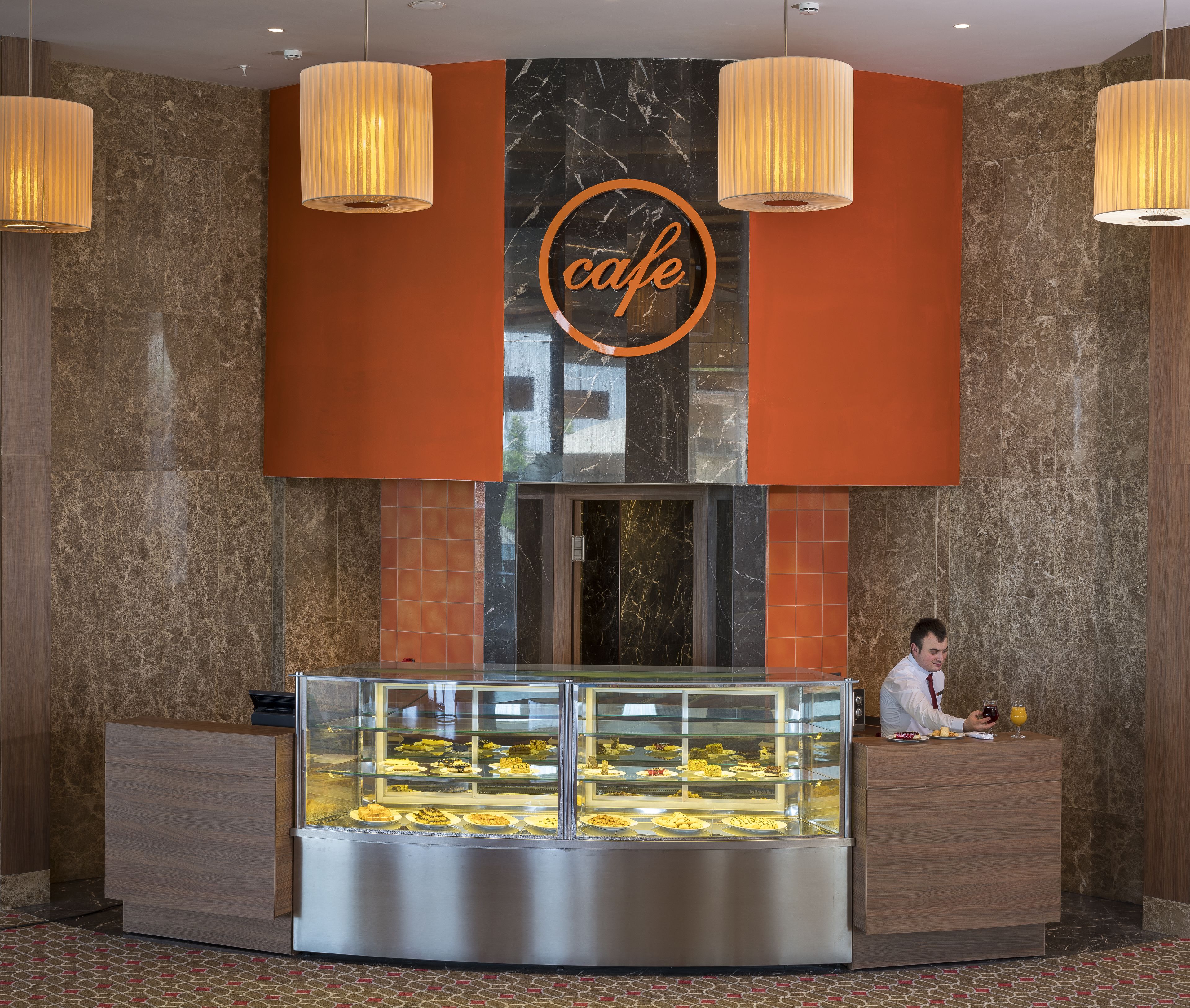 A cafe with a marble wall and a glass display case filled with pastries.