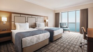A hotel room with two beds, a desk, and a view of the ocean.