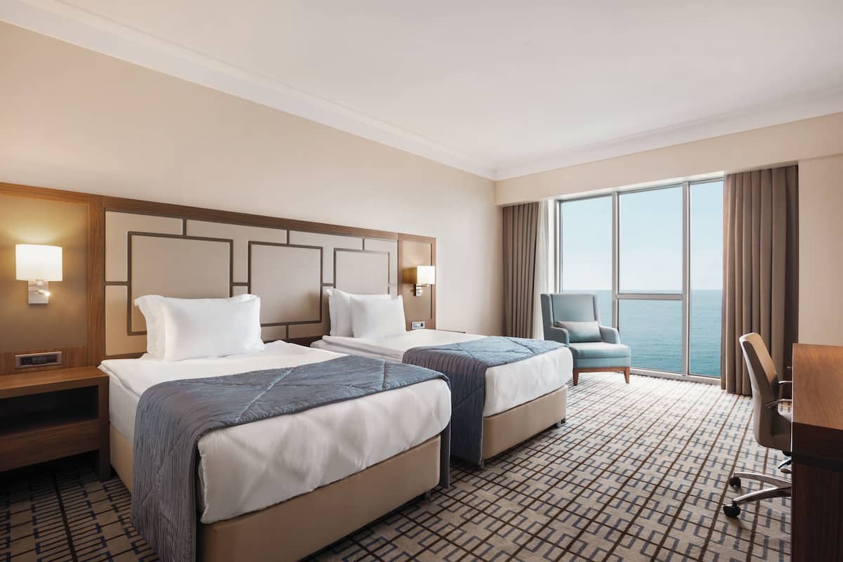 A hotel room with two beds, a desk, and a view of the ocean.
