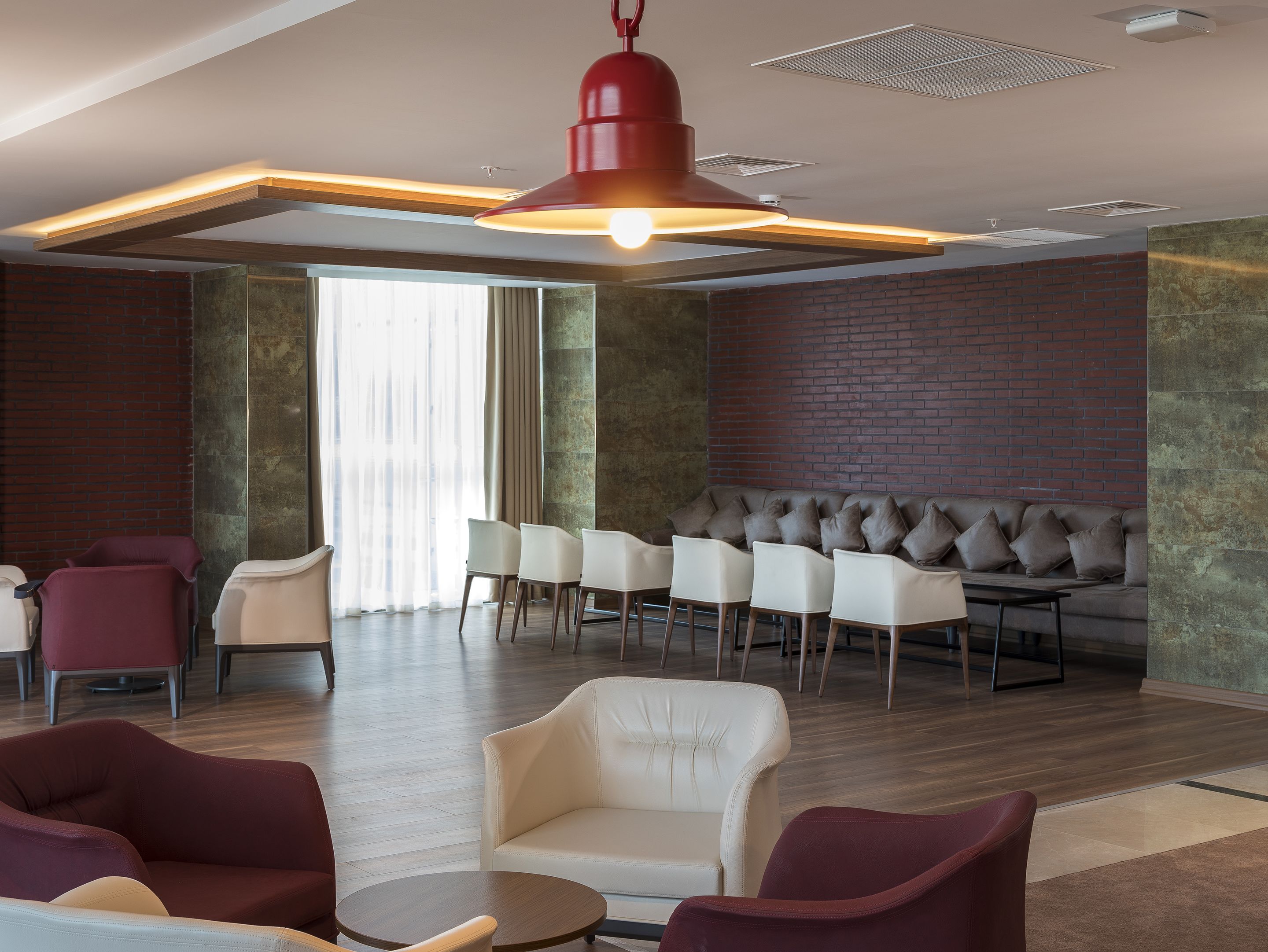 A modern lounge area with a seating arrangement, a red pendant light, and a brick wall.