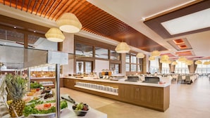 A modern buffet area with a central serving station, multiple food stations, and a spacious layout with natural light.