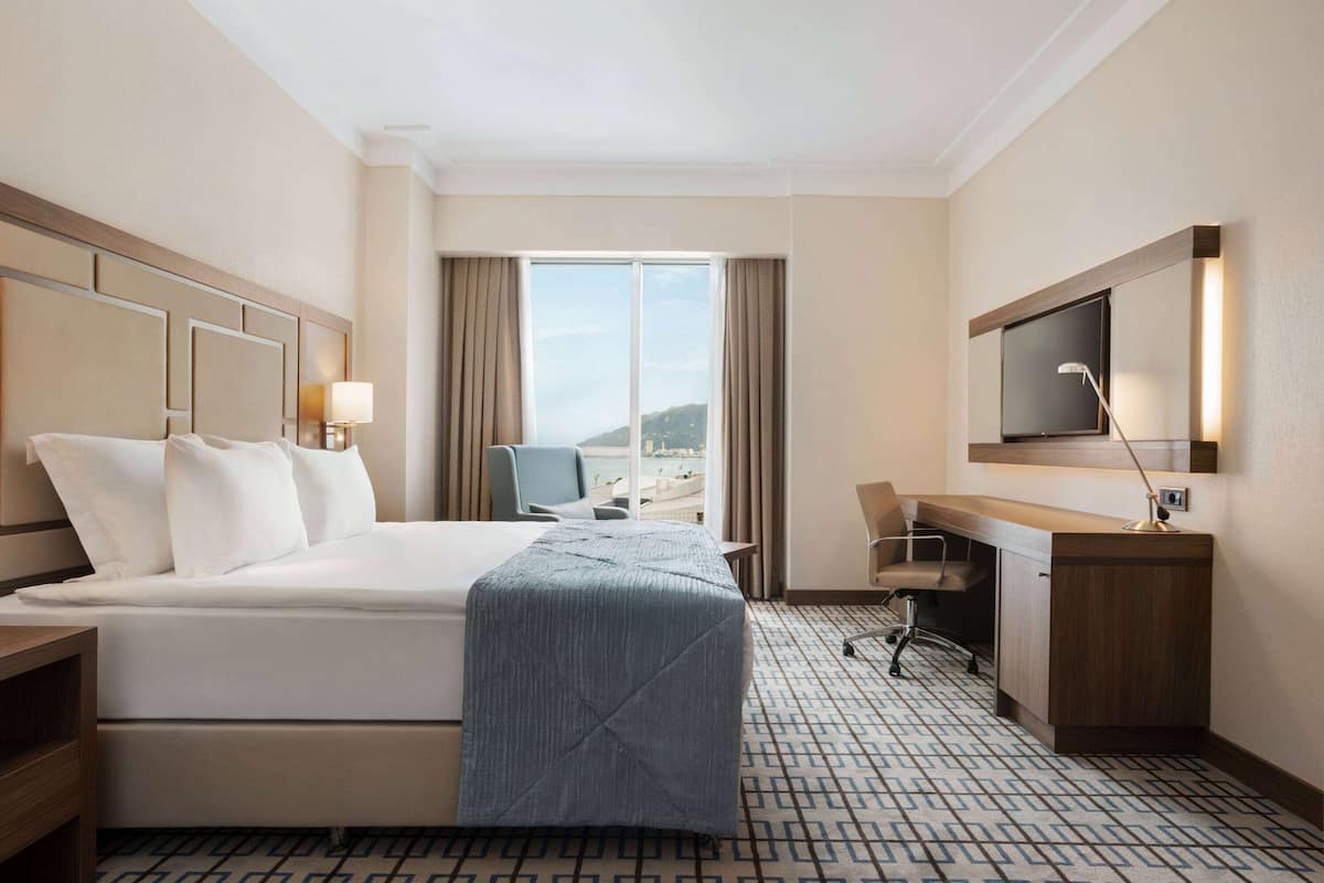 A hotel room with a large bed, a desk, a chair, a TV, and a window with curtains.