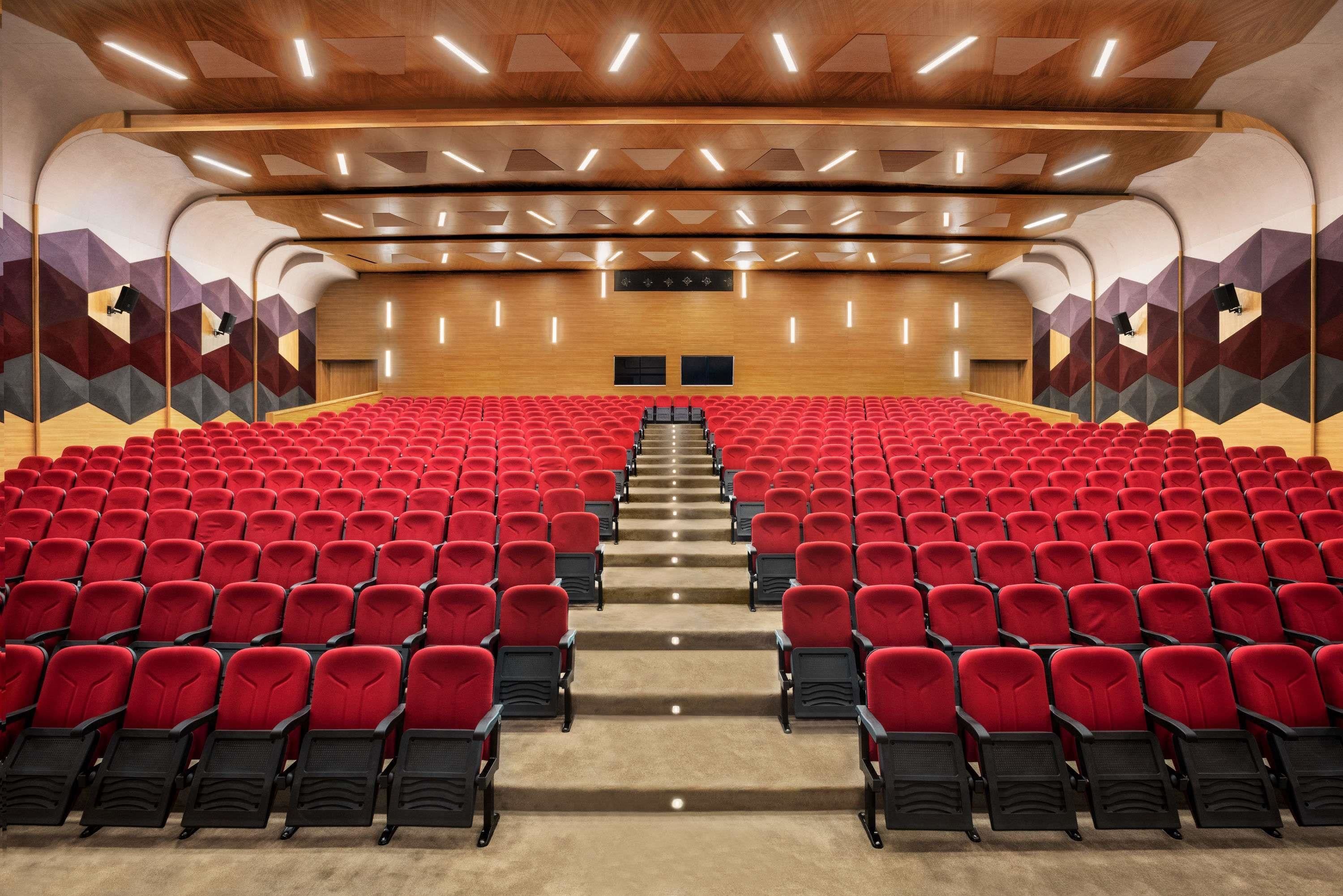 A theater with red seats, a wooden ceiling, and geometric wall designs.