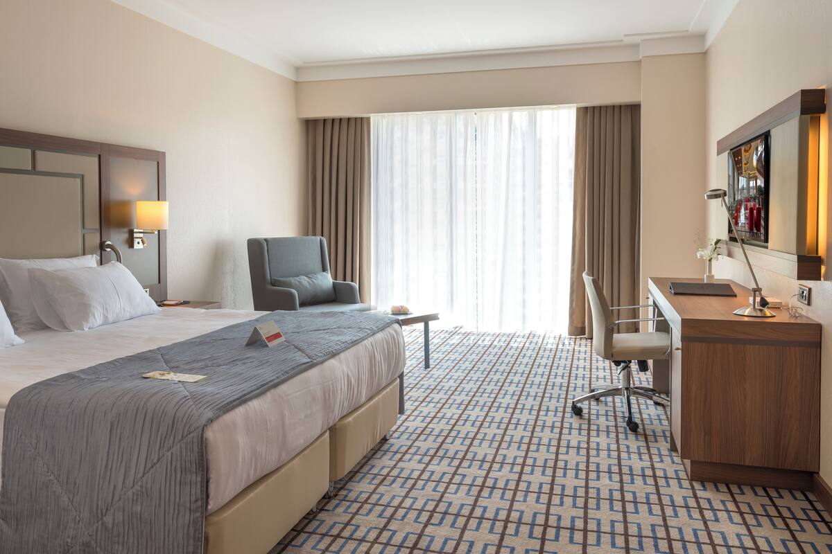 A hotel room with a bed, a desk, a chair, and a large window with curtains.