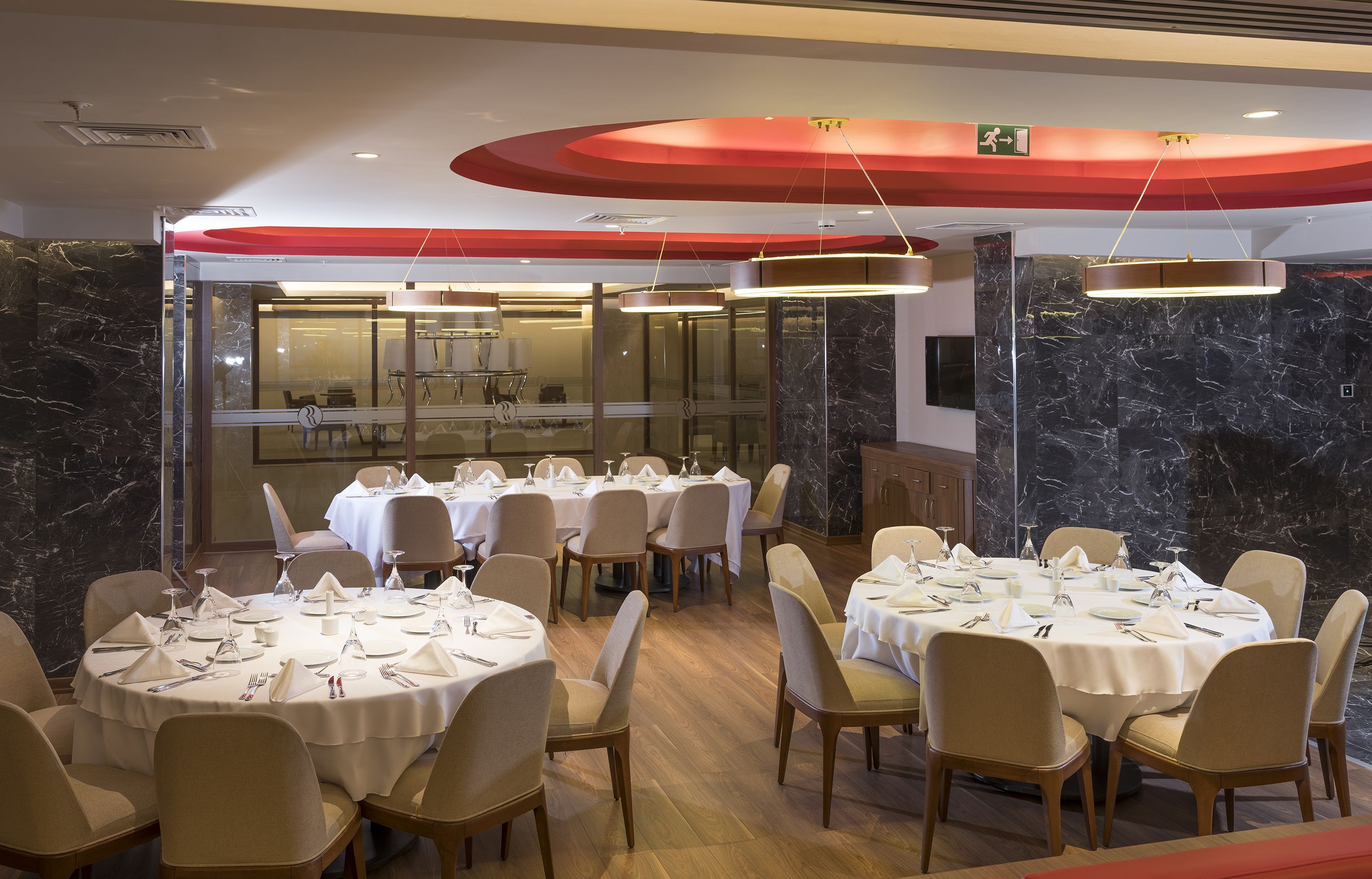 A dining area with round tables set for multiple guests, featuring white tablecloths and neatly arranged cutlery.