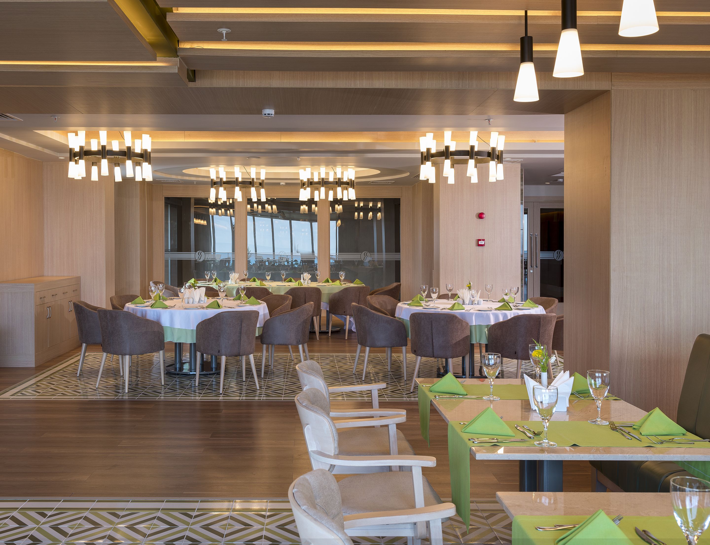 A modern dining area with multiple tables set for guests, featuring a geometric patterned floor and contemporary lighting fixtures.