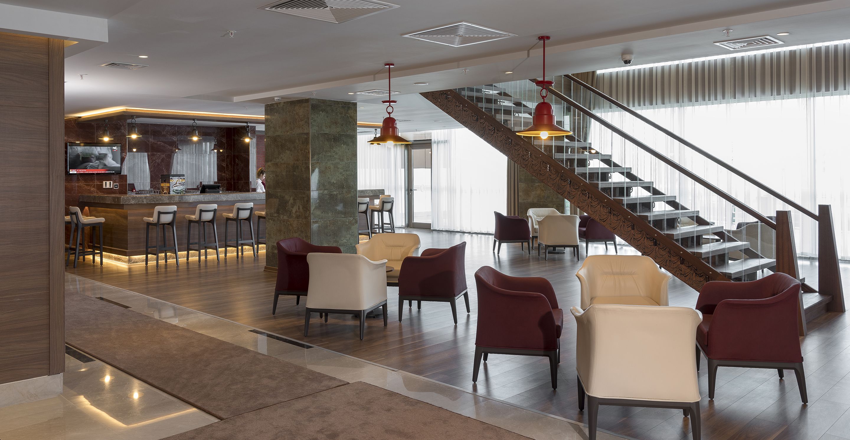 A modern hotel lobby with a bar area, seating, and a staircase.