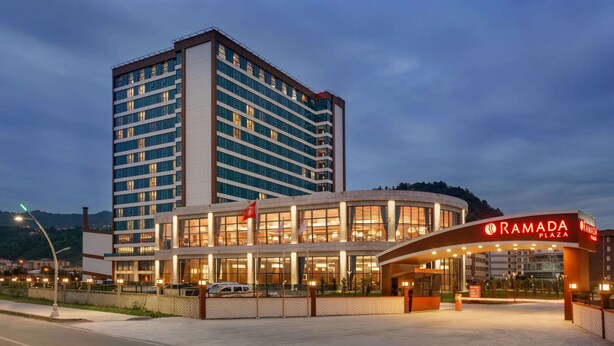 A modern hotel with a prominent "RAMADA PLAZA" sign, featuring a multi-story structure with large windows and a well-lit entrance area.