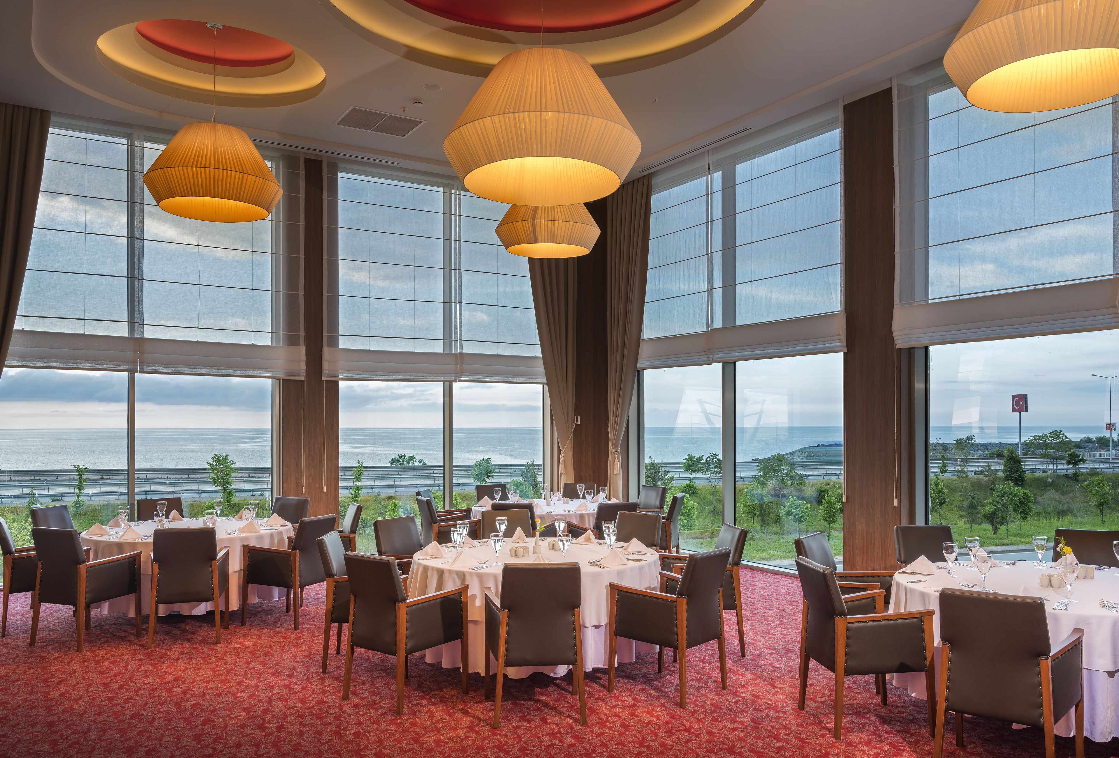 Un comedor con mesas redondas, sillas y ventanas amplias con vistas panorámicas.