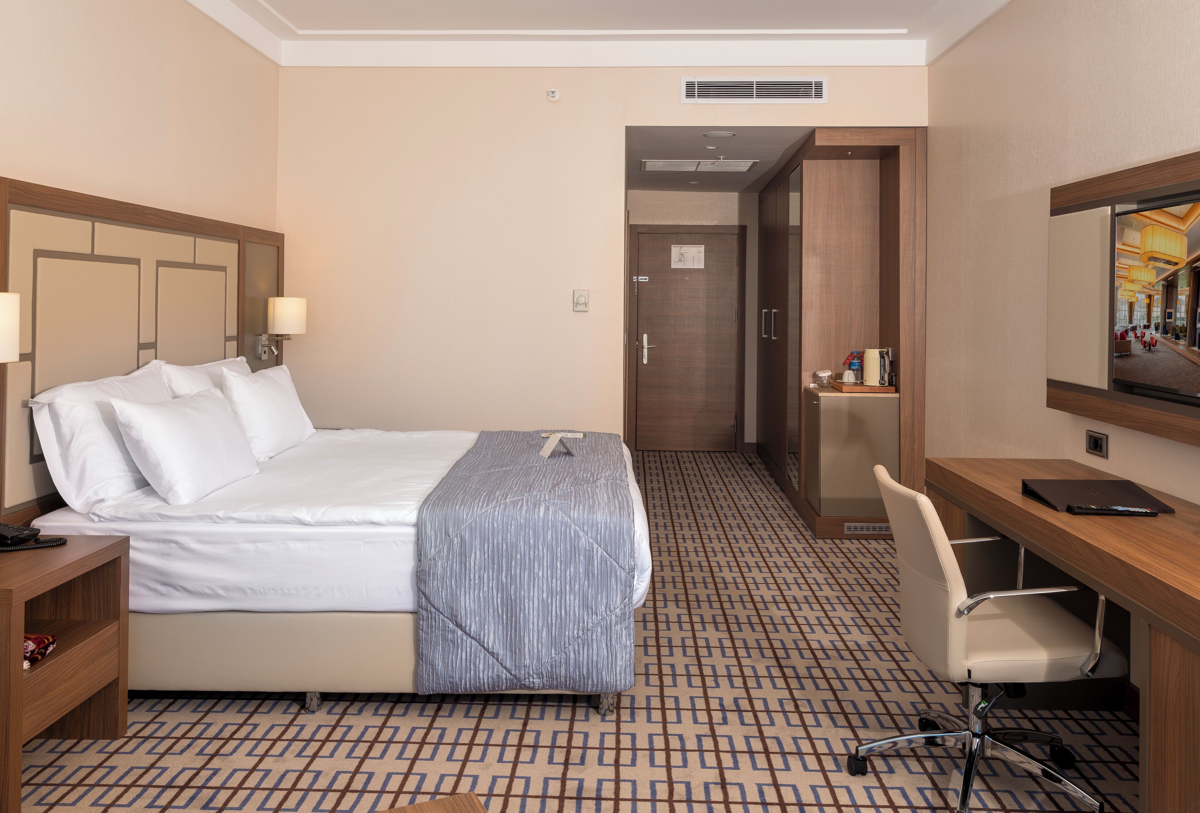 A hotel room with a bed, bedside table, chair, desk, and a large mirror.