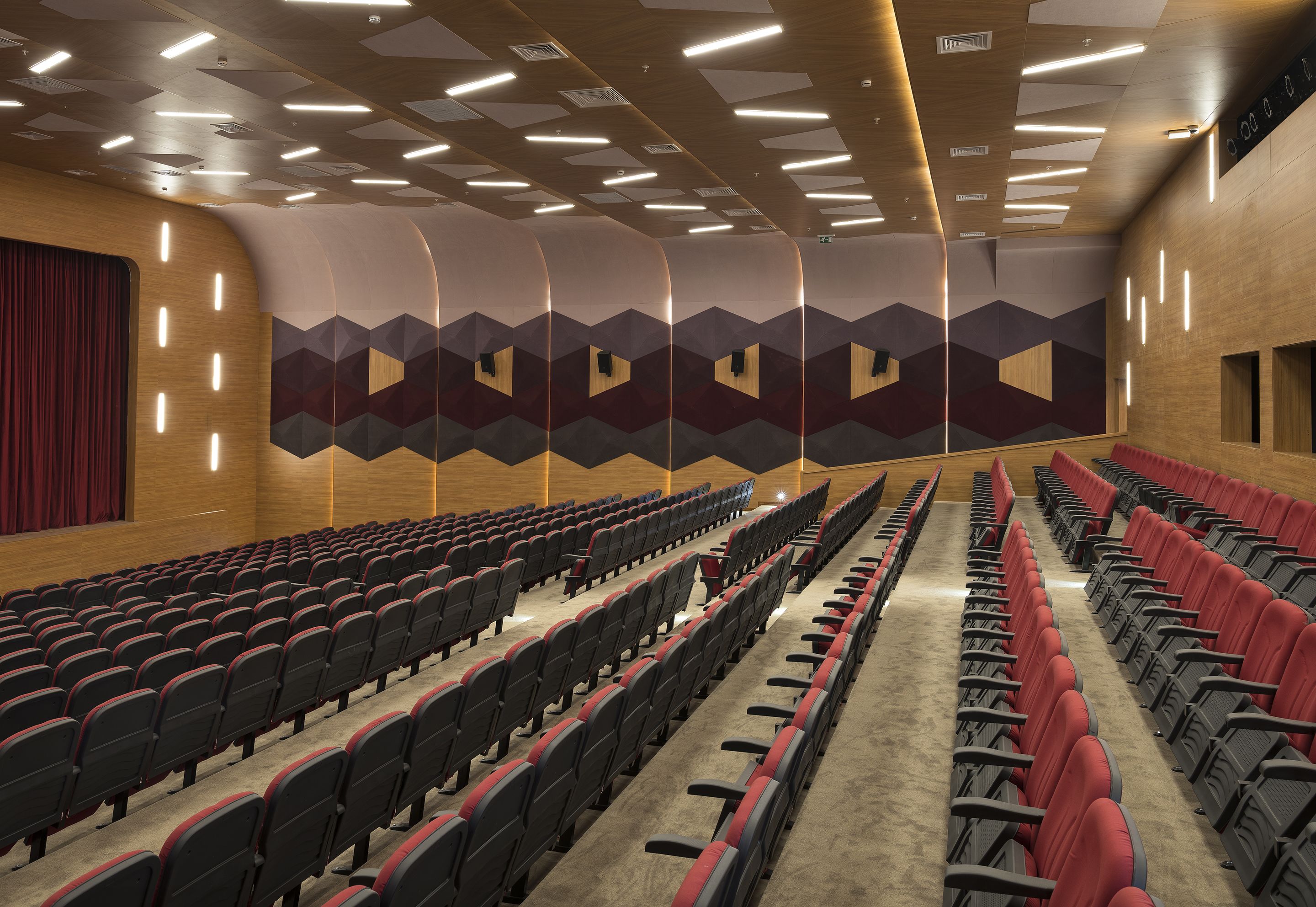 A theater with rows of red and black seats, wooden paneling, and geometric wall designs.