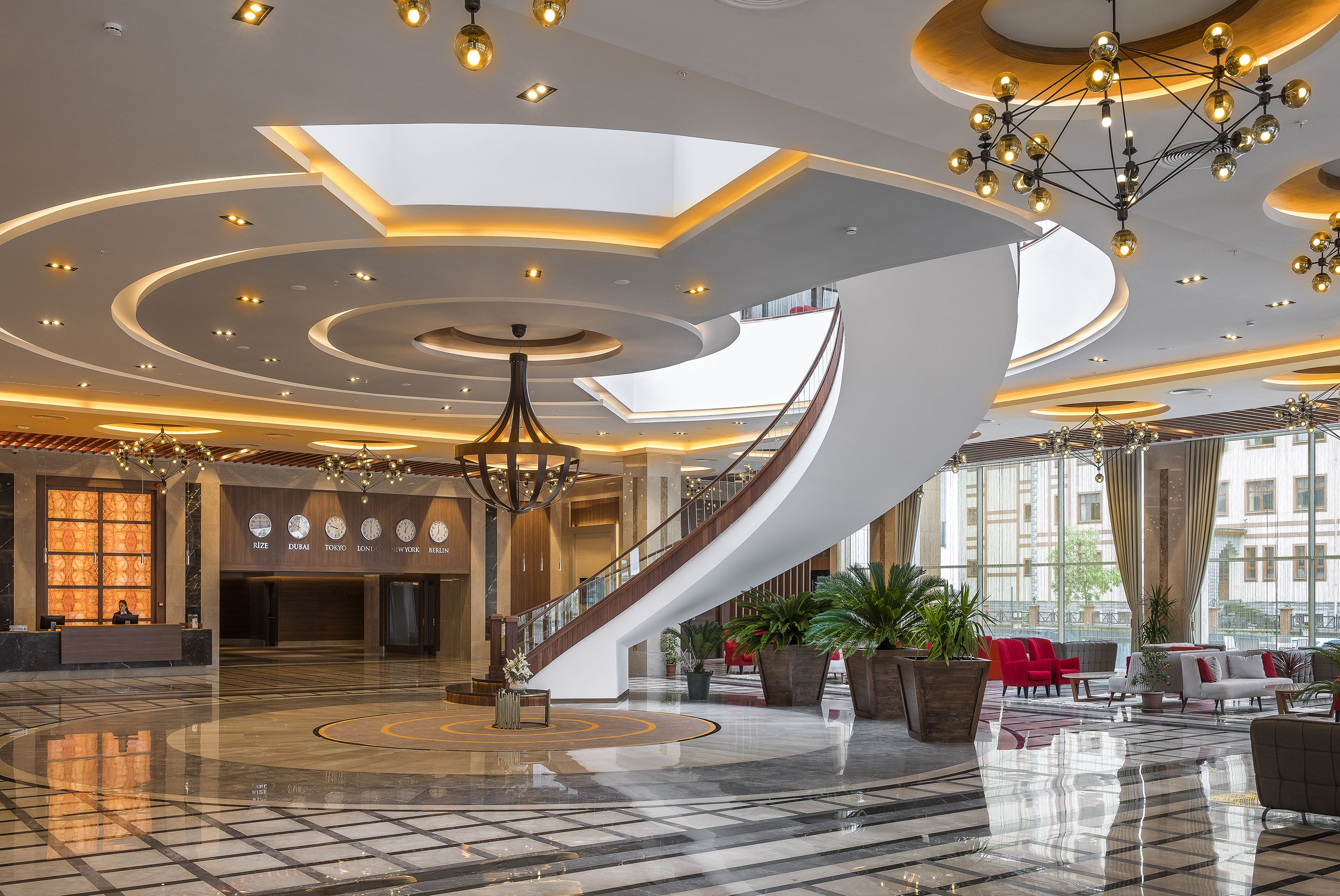 A spacious lobby with a central staircase, modern lighting fixtures, and seating areas.