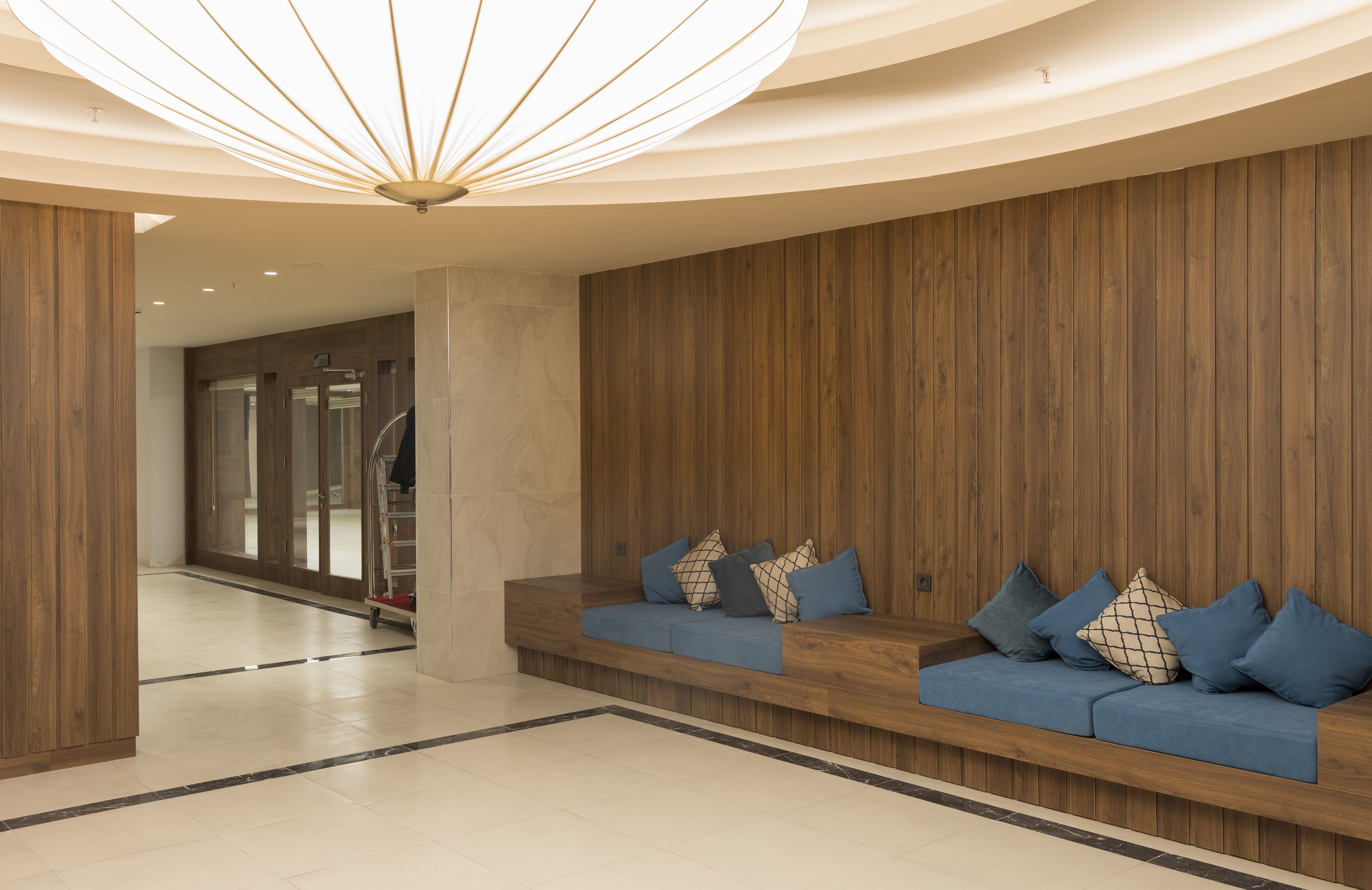 Un hall d’entrée moderne avec un comptoir d’accueil en bois, un canapé bleu agrémenté de coussins et un luminaire au plafond au design original.