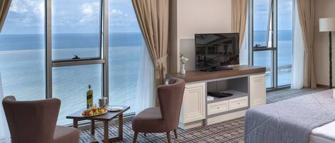 A hotel room with a large window, a desk, two chairs, a bed, and a TV.